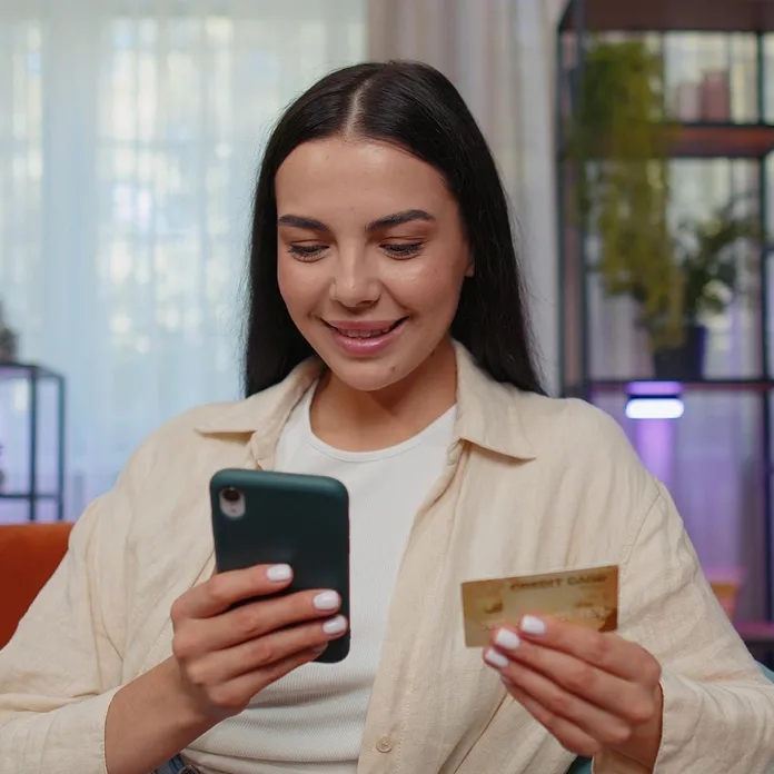 Girl smiling while checking her phone and holding a bank card