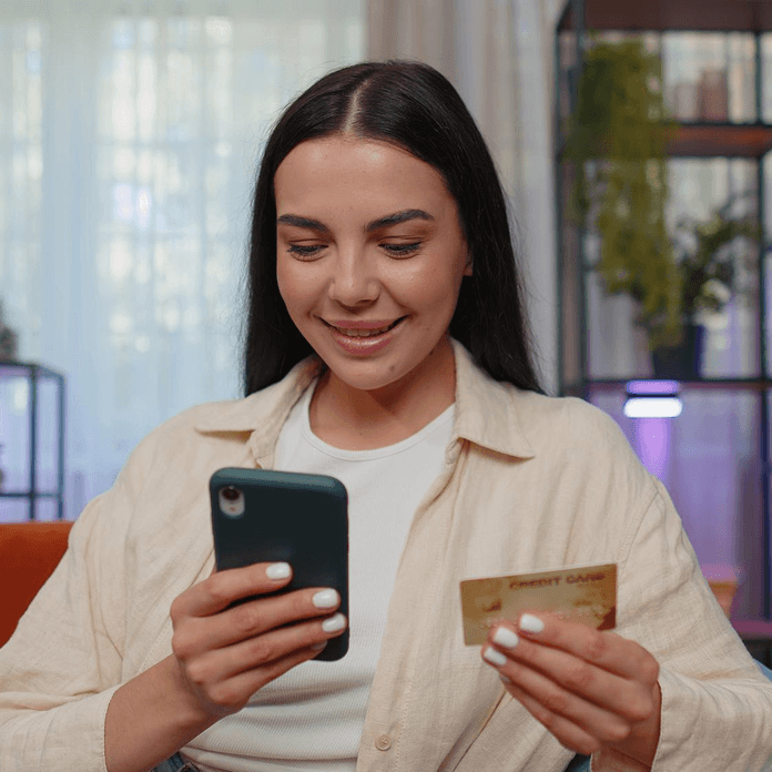 Girl smiling while checking her phone and holding a bank card